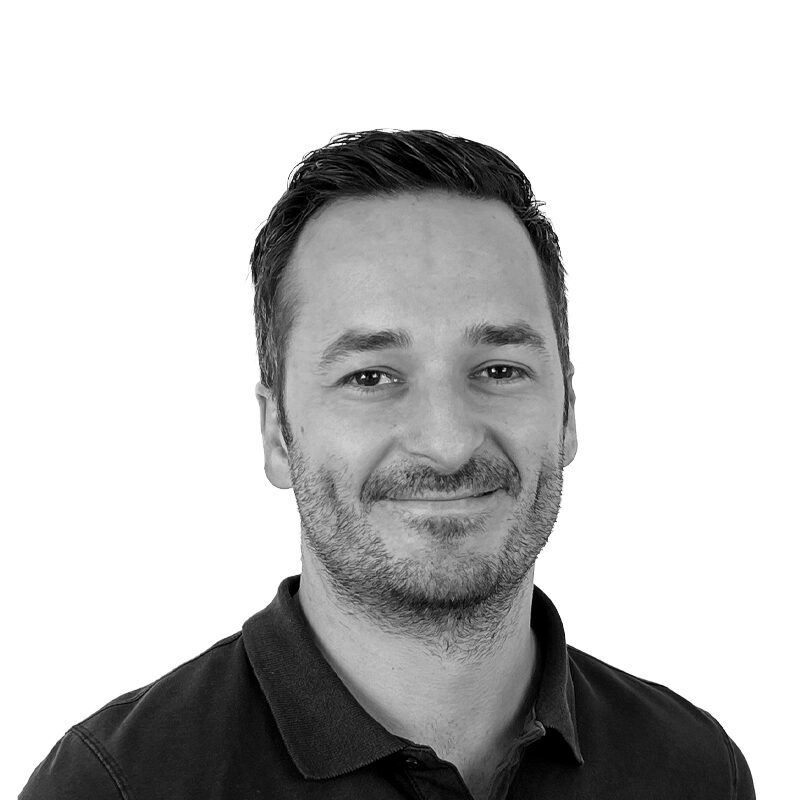Black and white portrait headshot of a smiling man with short hair and light stubble, facing the camera.